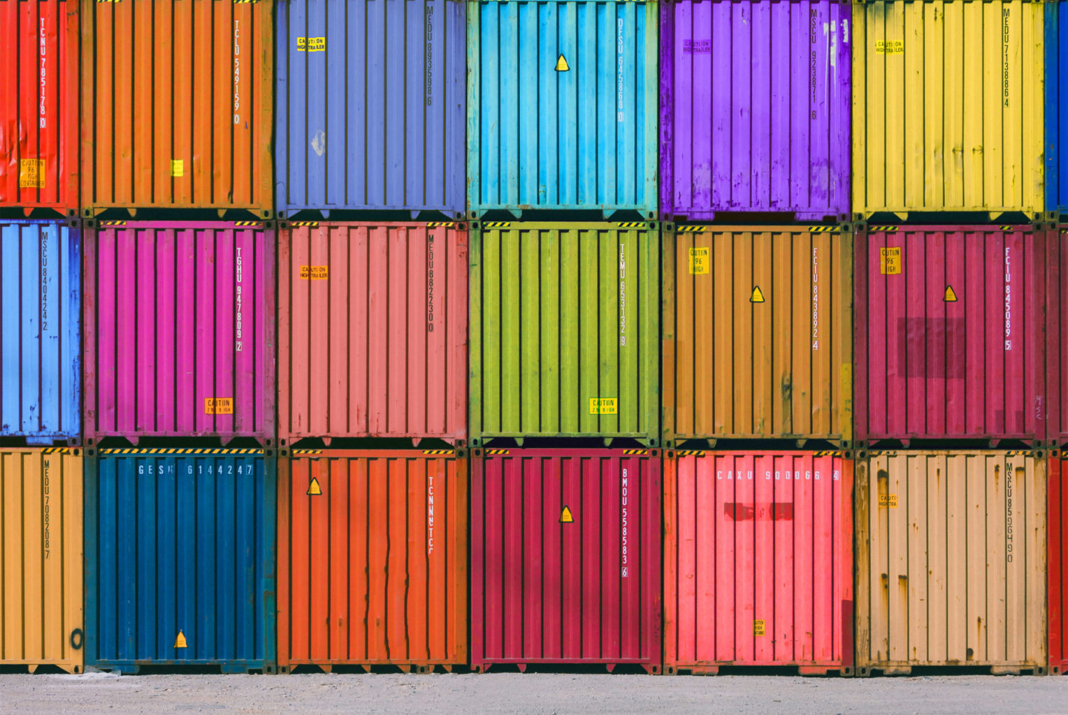 Engineer man with yellow crash helmet and worker west checking cargo freights in front of colorful cargo container stacks in shipping port