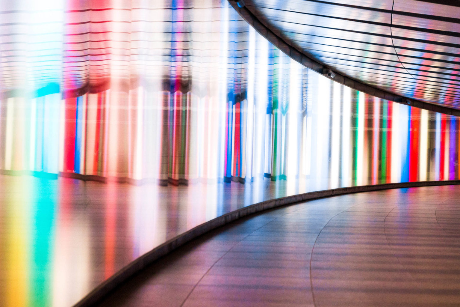 Wide angle color image depicting the front view of a young woman walking through a futuristic subway tunnel in central London, UK. The tunnel is illuminated with multi colored lights. The woman is in the far distance, and the focus is on the cool science fiction architecture of the subway tunnel that curves round into the distance. Room for copy space.
